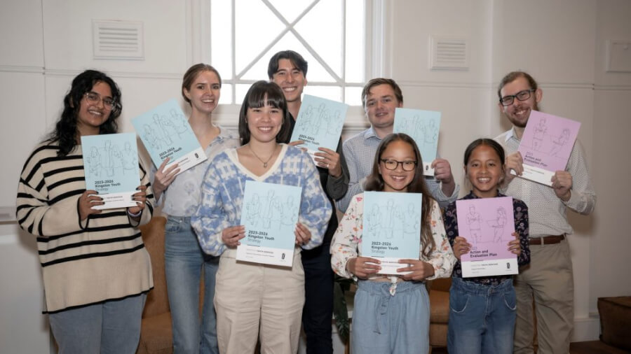 Young people holding in front of them the hard copy version of the 2023 - 2026 Kingston Youth Strategy and Action Plan.